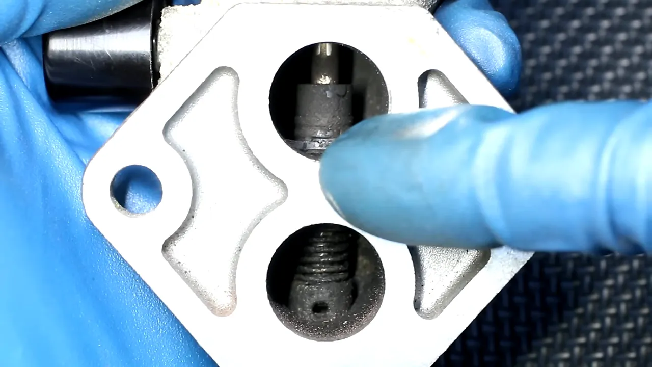 Close-up of an idle air control valve with dark deposits inside its two circular passages