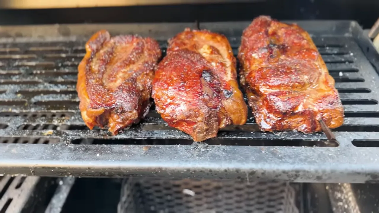 Three browned pork steaks on the upper rack with a charcoal basket below