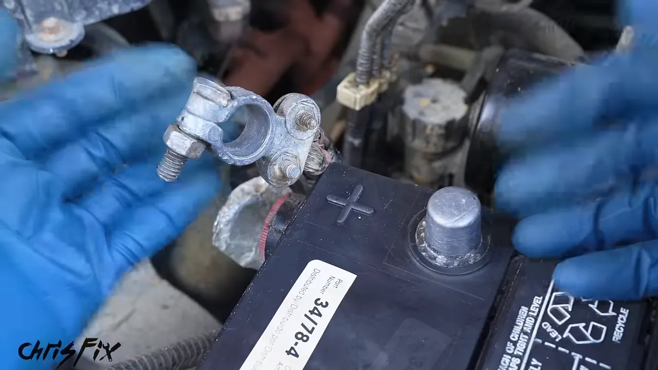 Gloved hands holding a cleaned battery cable clamp beside a battery post