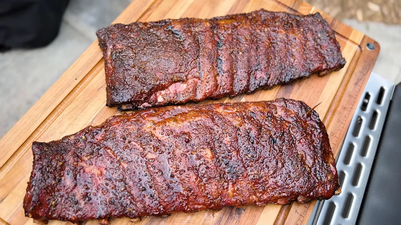 Two cooked racks of ribs with dark bark resting side by side on a wooden cutting board