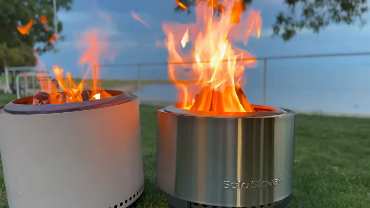 White Bonfire on the left and shorter stainless steel Summit on the right, both burning at dusk