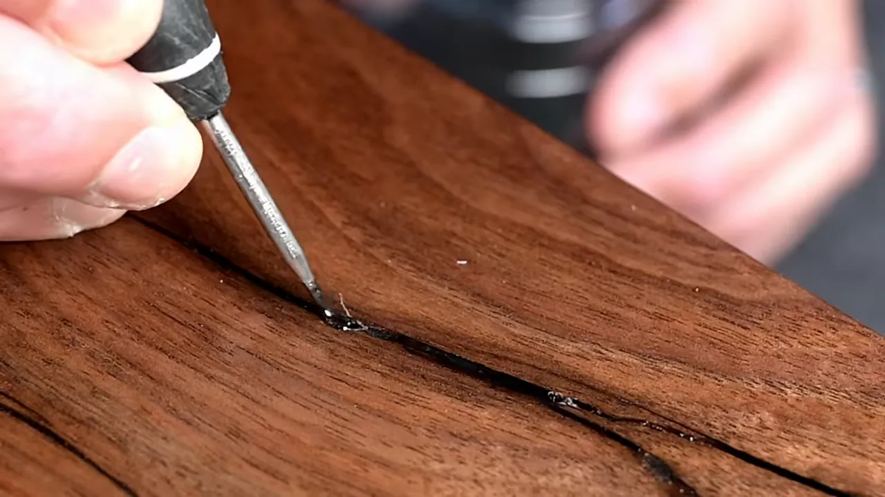 Fine applicator placing black glue into a narrow crack in the finished walnut