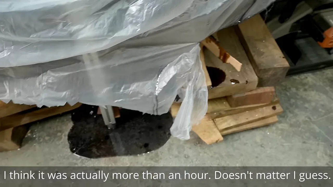 Black epoxy puddle on the floor beneath a plastic-covered workbench