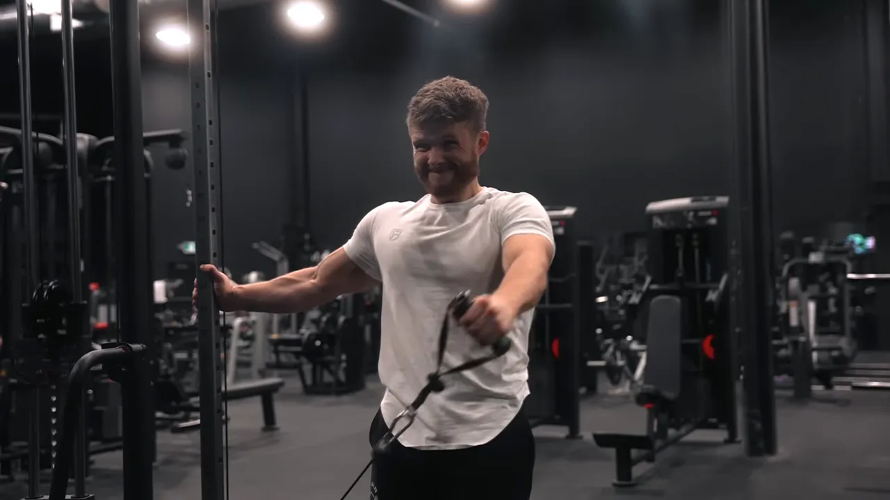 Lifter raising a cable handle diagonally outward with one arm while holding the machine with the other