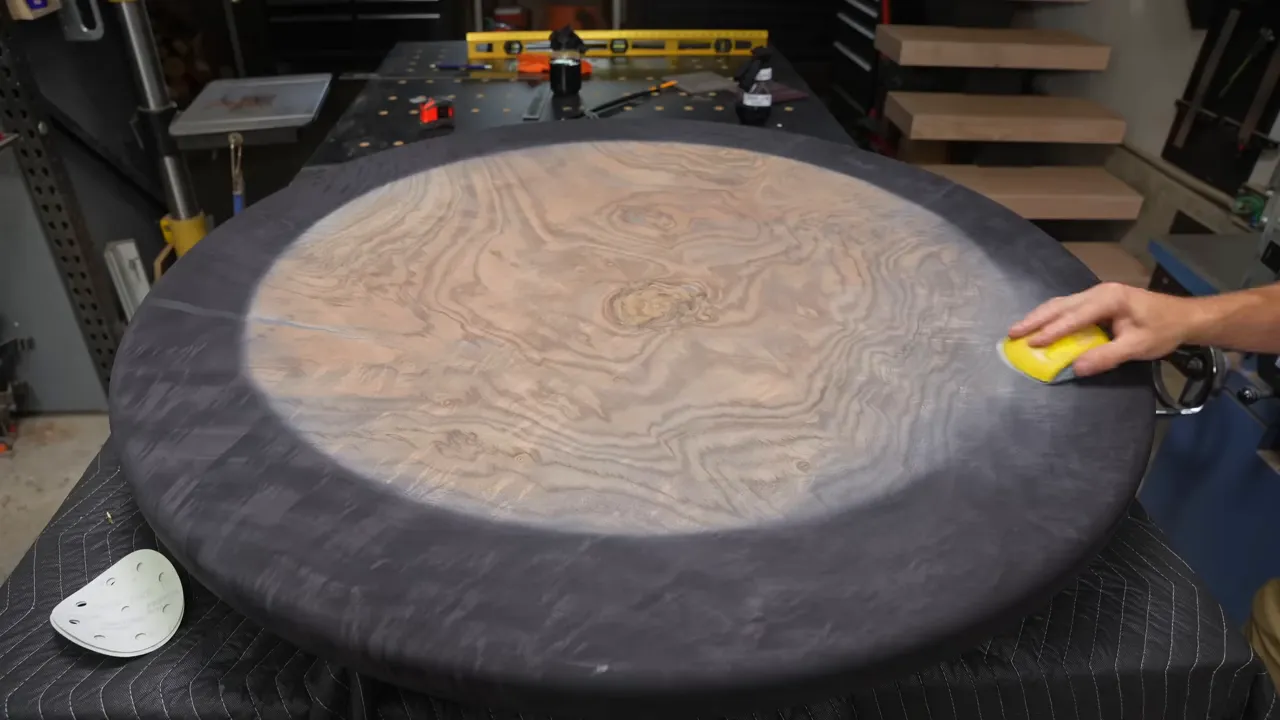 Round walnut tabletop with a pale center and dark perimeter during hand sanding