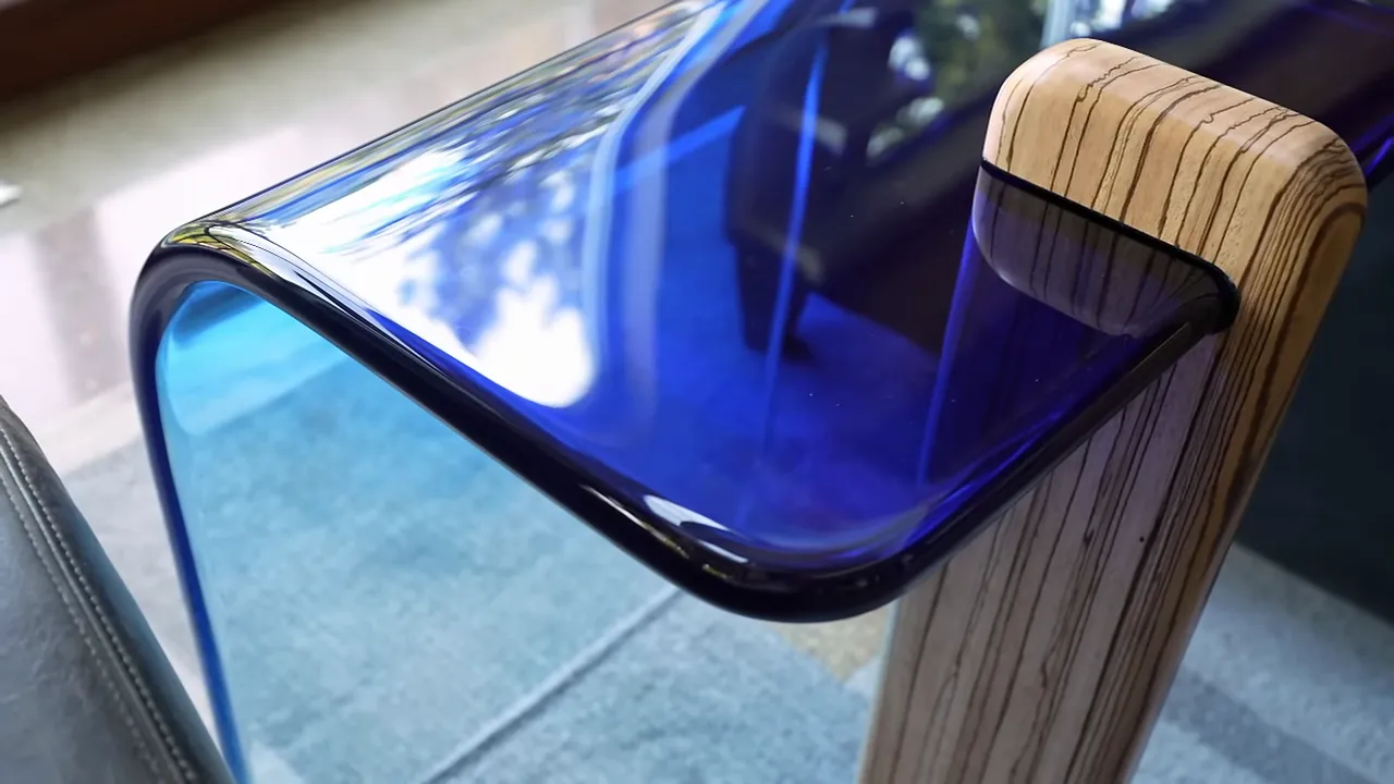 Polished blue epoxy end table with a curved body and single zebrawood support beside a dark chair