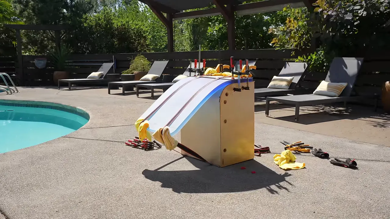 Blue epoxy slab bent partway around an outdoor wooden form with yellow ratchet straps