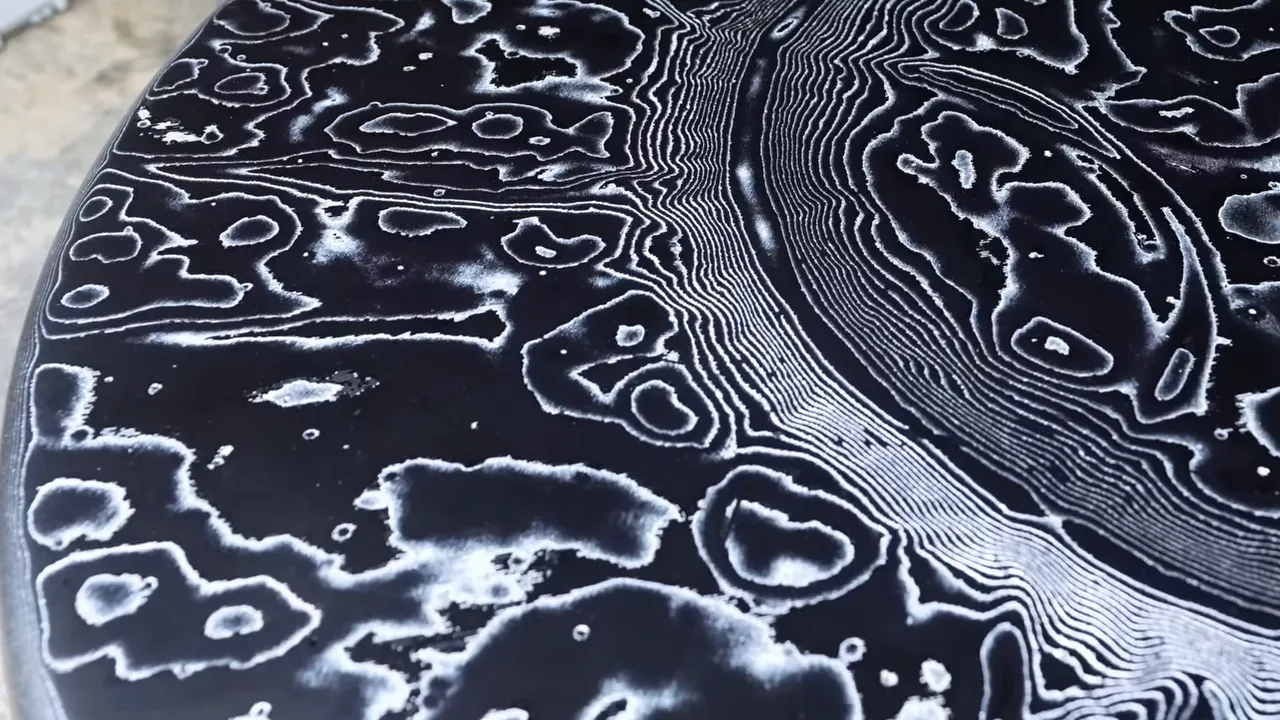 Close-up of a black circular tabletop with silver contour-like lines and a broad circular pattern