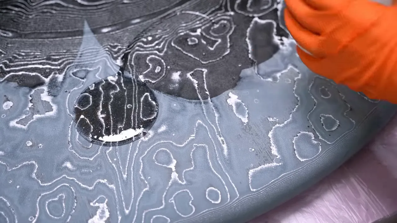 Gloved hand spreading clear epoxy over black denim with bright winding silver lines