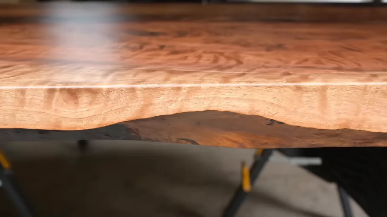 Finished walnut tabletop with a natural live edge above sculptural metal legs