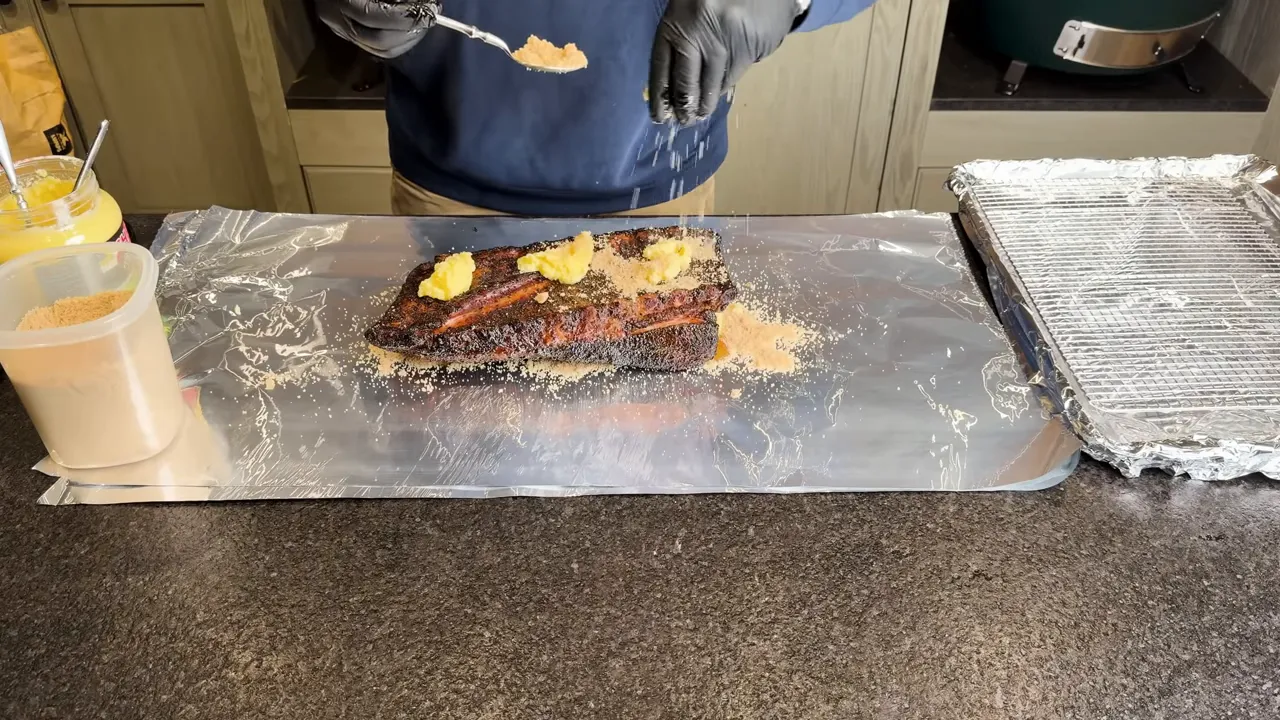 Smoked rib rack on aluminum foil with clarified butter and brown sugar on the bone side