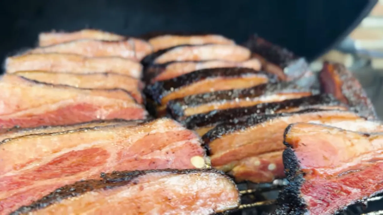 Individual bacon ribs on the grill showing pink cut faces and dark bark