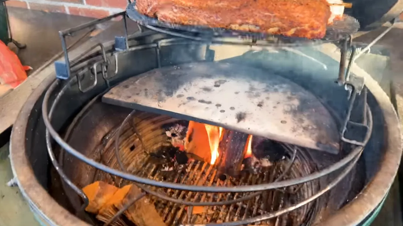 Live wood fire beneath heat deflectors and an elevated cooking rack inside a Big Green Egg