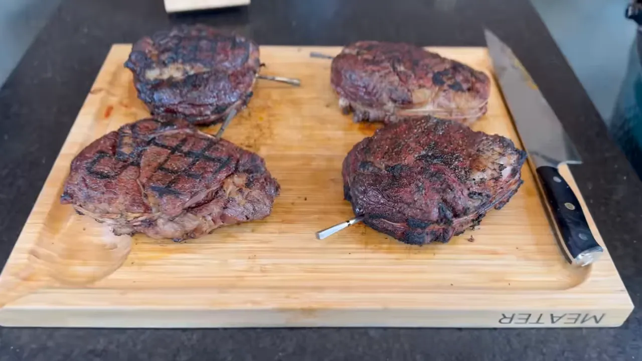 Four cooked steaks with different surface browning and grill marks on a wooden board