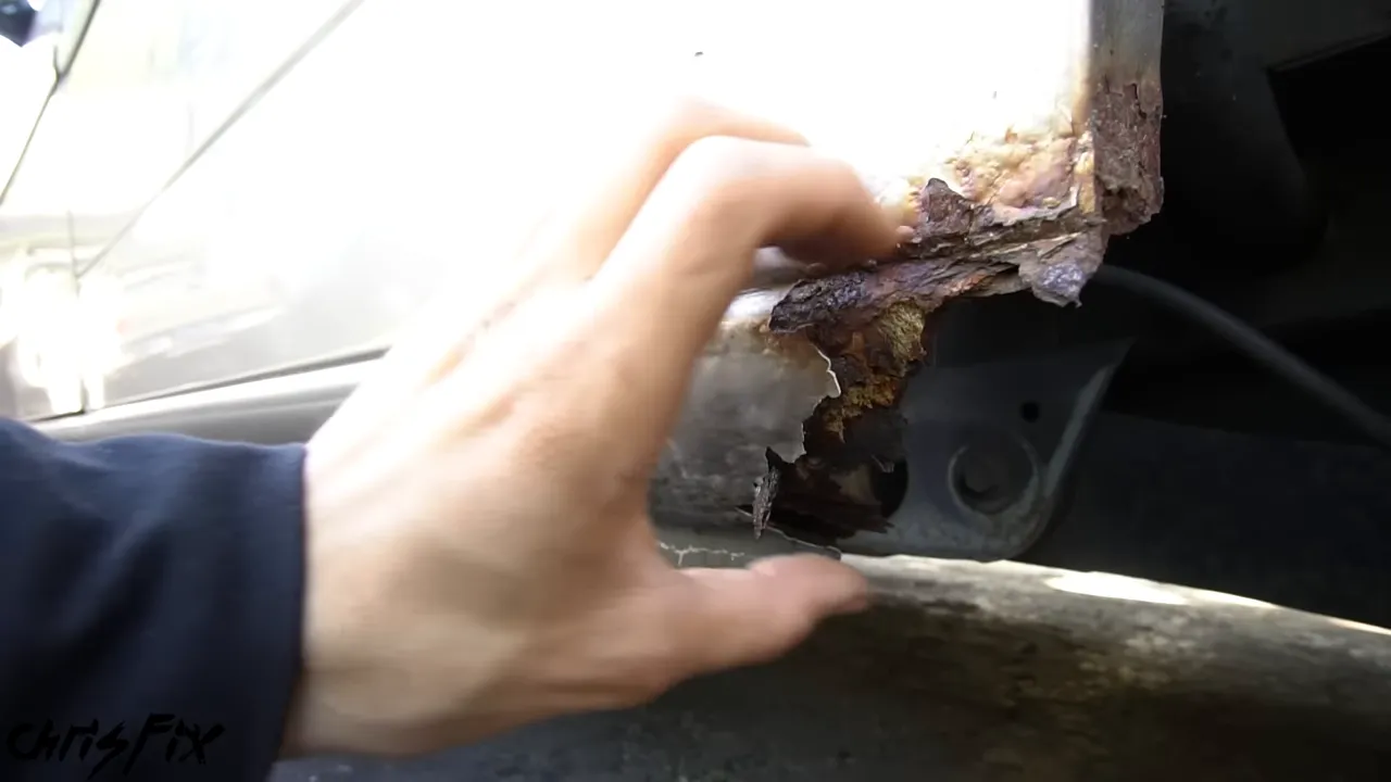 Severely rusted lower body panel with a large section missing beside the rear wheel