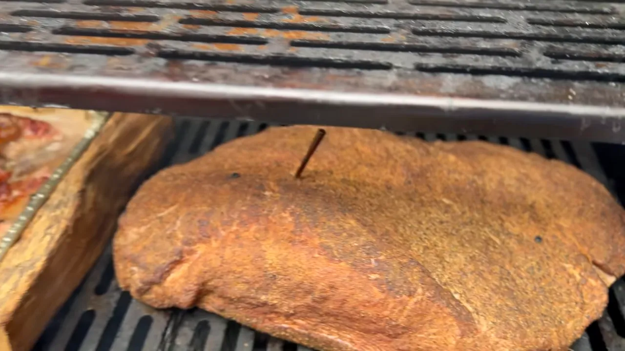 Brisket on the right grate beside a wood split and a pan of beef trimmings on the left
