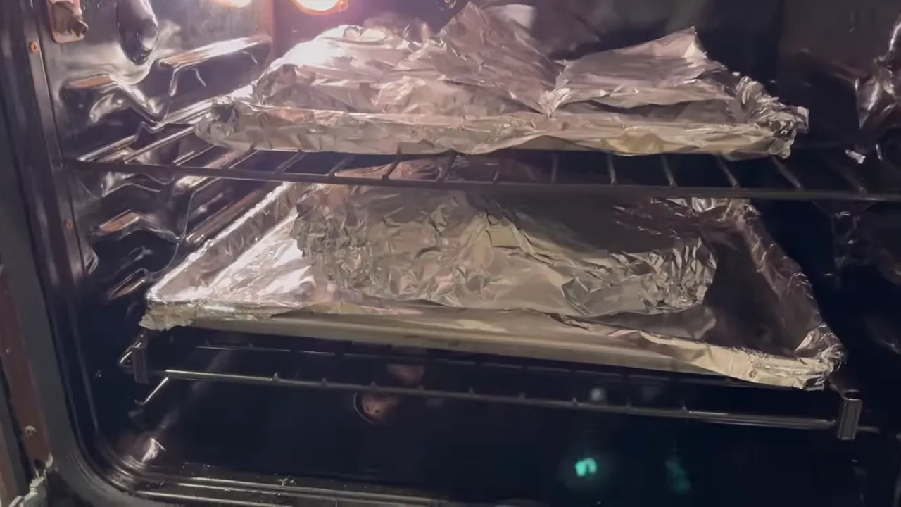 Foil-wrapped food packages resting on trays on two oven racks