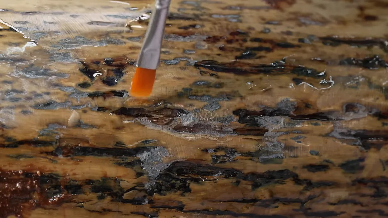 A small brush applying brown filler to pits in the mottled tusk surface