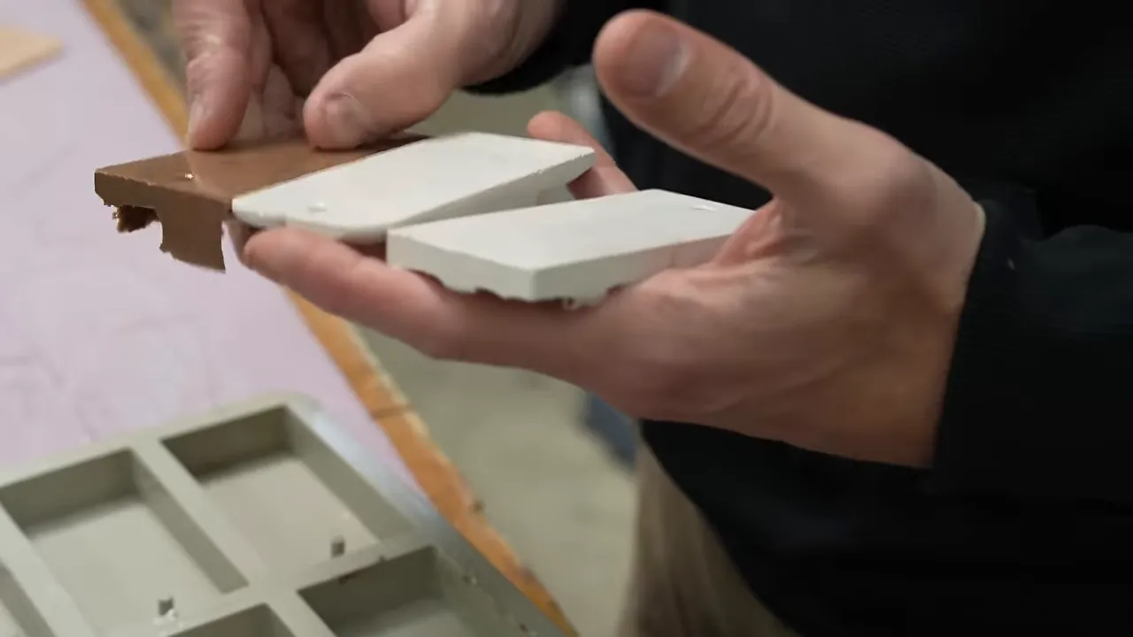 Hands holding pale and brown rectangular repair samples beside small molds