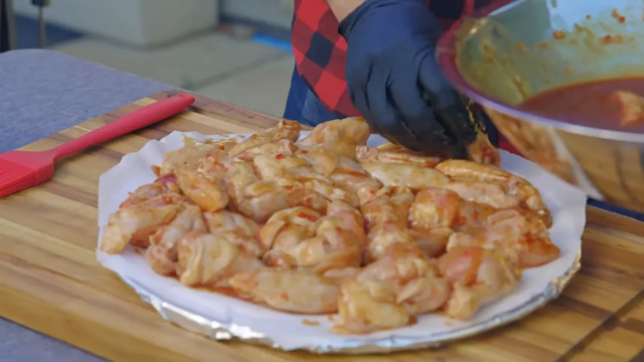 Marinated chicken wings arranged on a parchment-lined round tray beside a bowl of sauce
