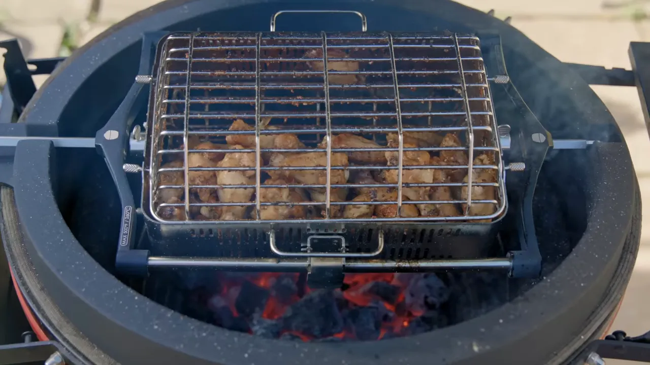 Rotisserie basket of chicken wings positioned above glowing charcoal in an open kamado grill