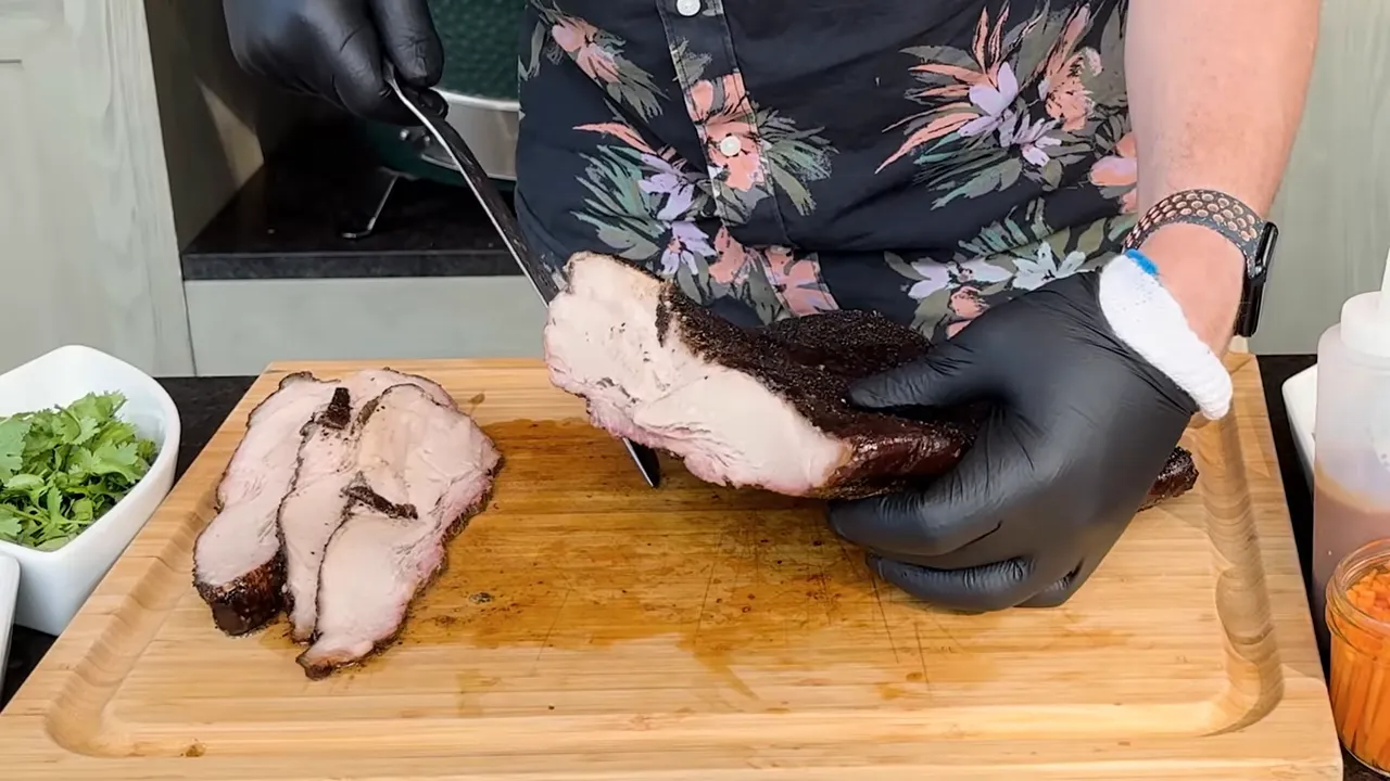 A slice of smoked pork belly held above a cutting board beside several intact slices
