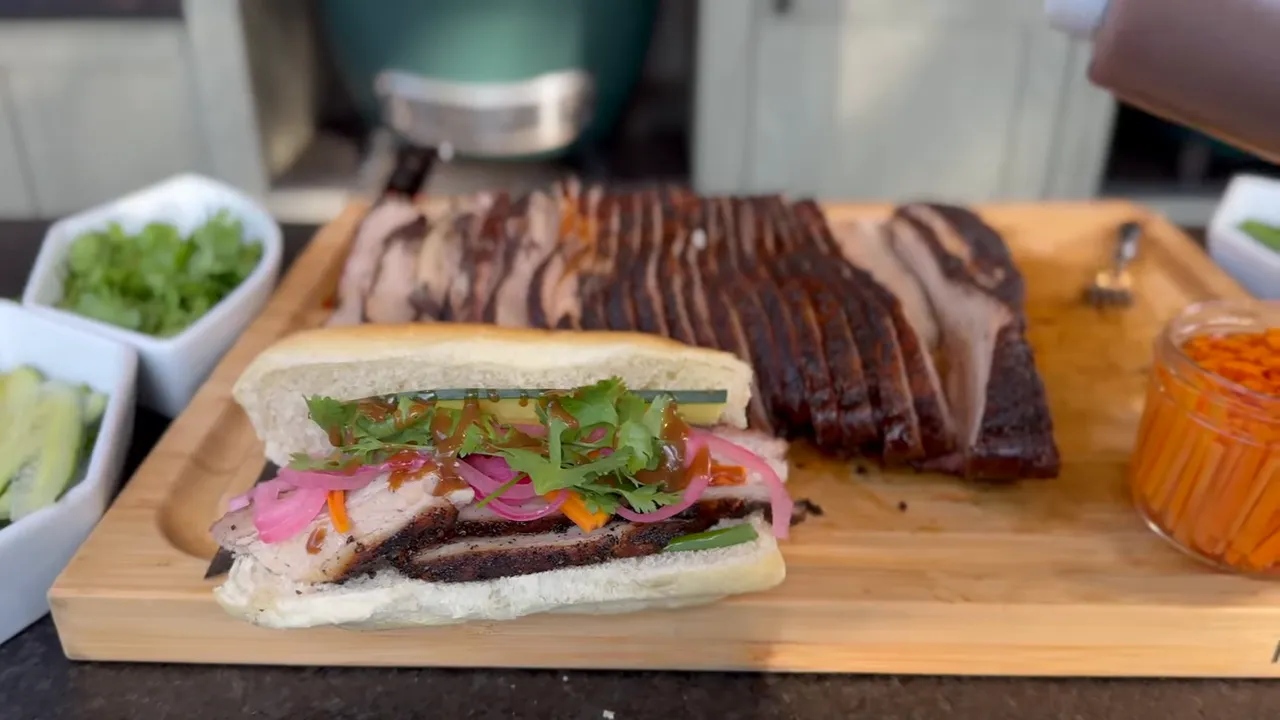 Pork belly sandwich with pickled vegetables and cilantro beside sliced pork belly