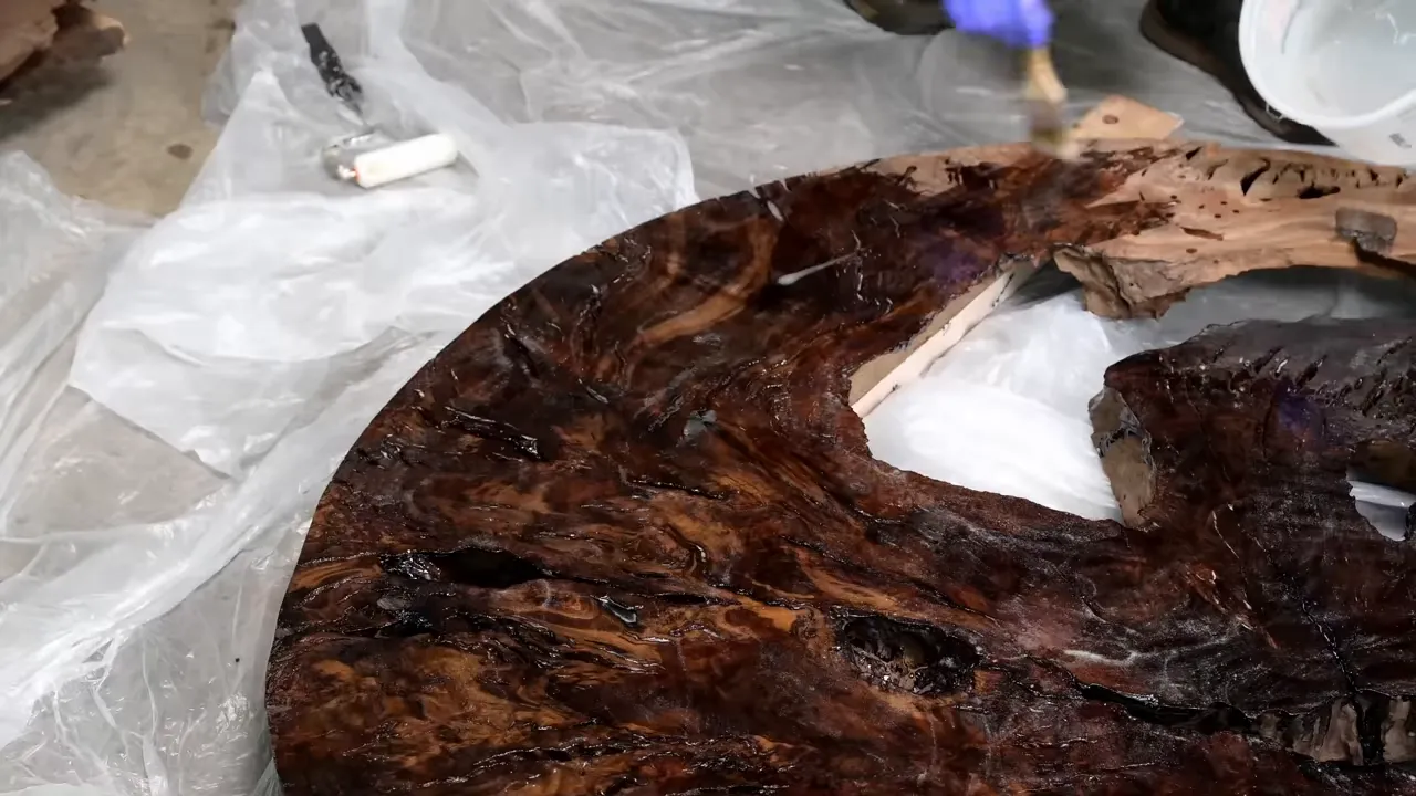 Gloved hand brushing clear epoxy along a large void in the walnut cookie