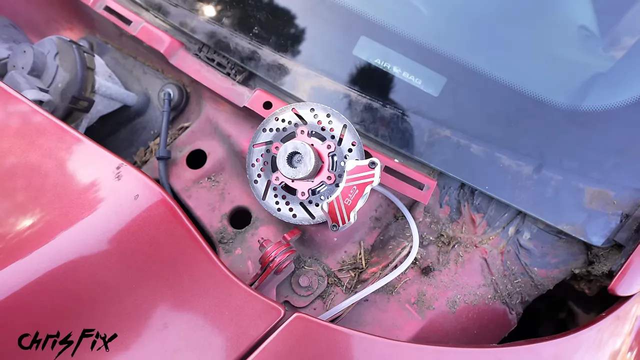 Miniature drilled rotor and red caliper mounted beneath the Mustang windshield with the cowl removed