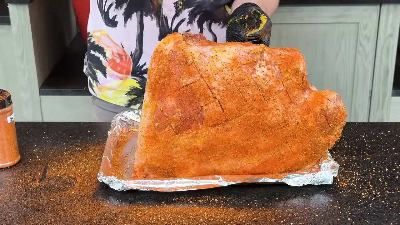 Seasoned pork shoulder resting on a foil-lined tray beside two seasoning containers
