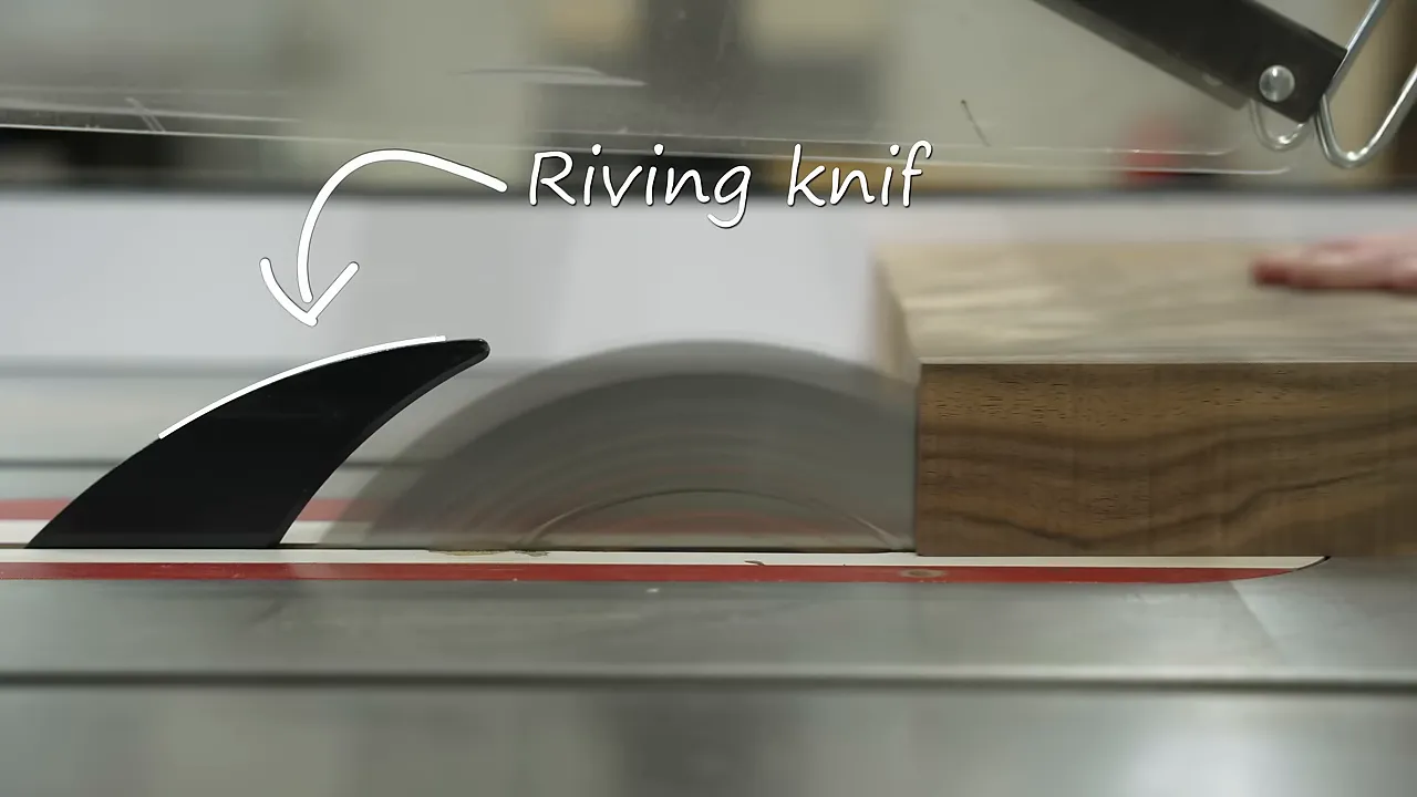 Labeled riving knife behind a spinning table saw blade as a board approaches