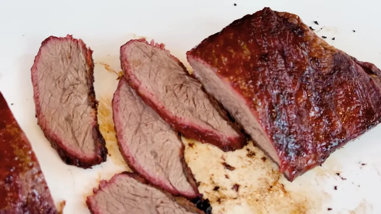 Sliced cooked tri-tip on a white cutting board with brown interiors, pink edges, and visible pale fat