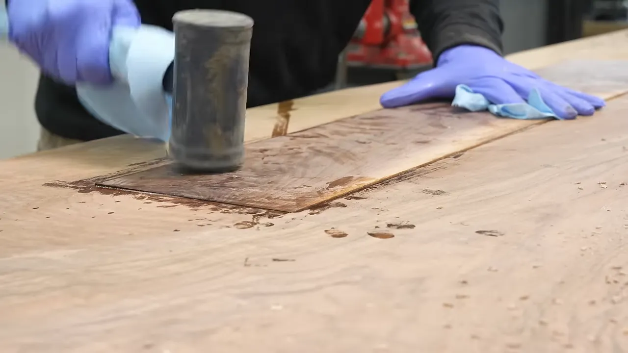 A rectangular wood patch being seated into the underside of a walnut tabletop