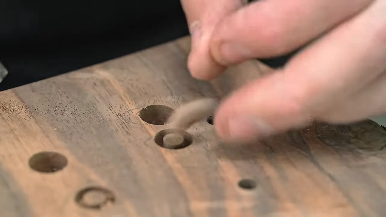 Hands lifting a small wood plug from a board with circular plug cuts