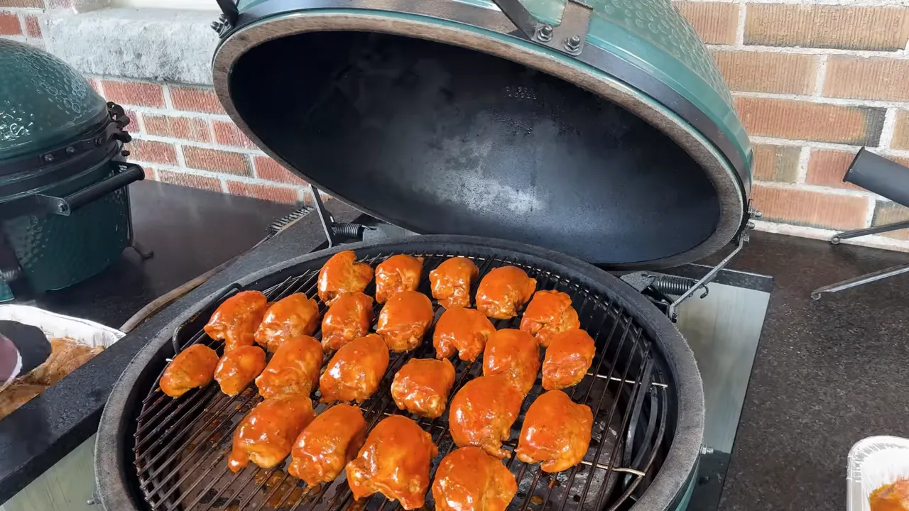 Sauce-coated chicken thighs arranged on the lower grate of a Big Green Egg
