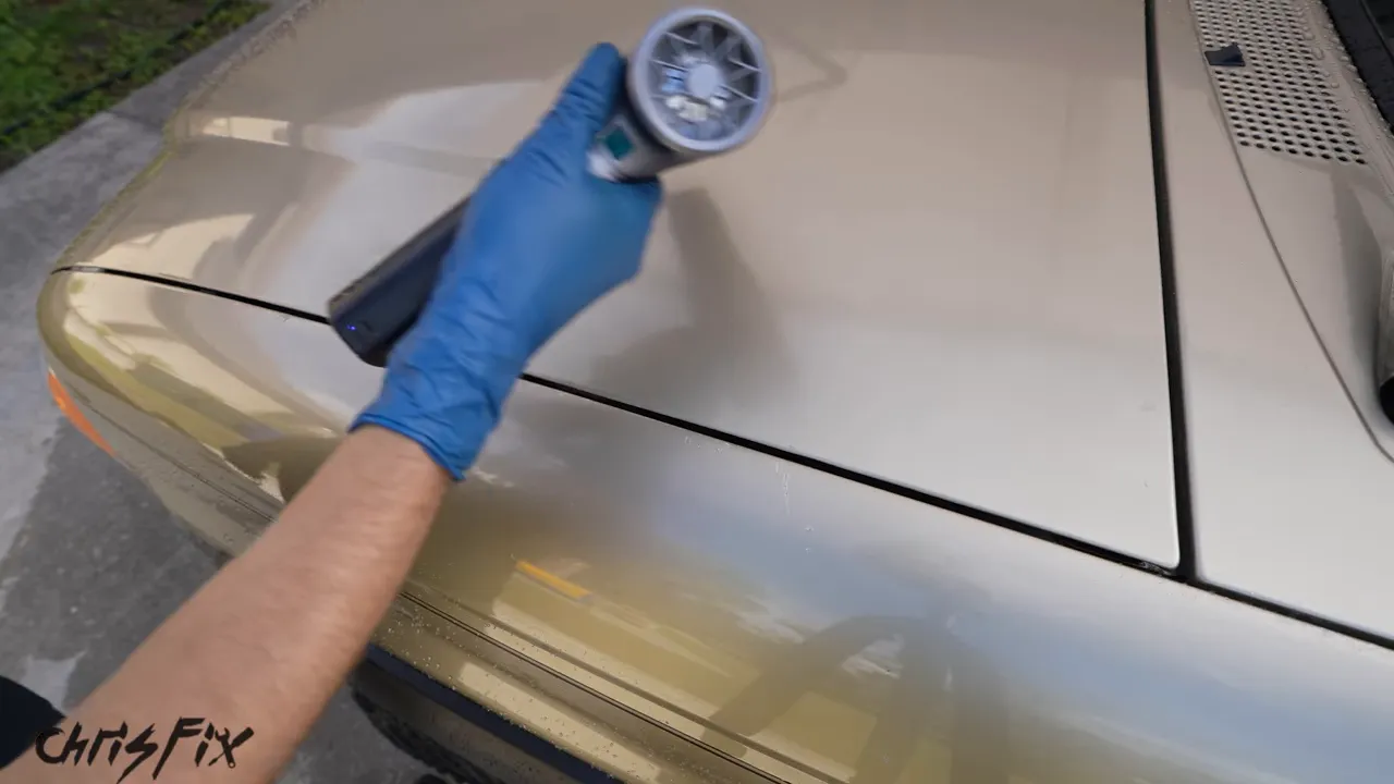 Handheld air blower pushing water across a car hood