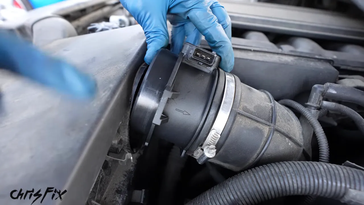 Gloved hand pointing to the airflow direction arrow on the mass airflow sensor housing