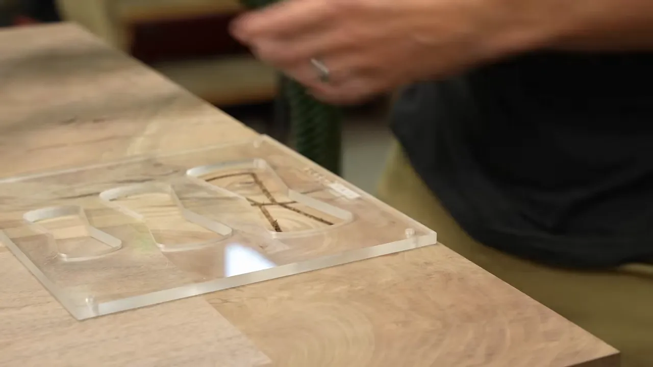 Clear acrylic bow tie template positioned over a routed outline across a walnut crack
