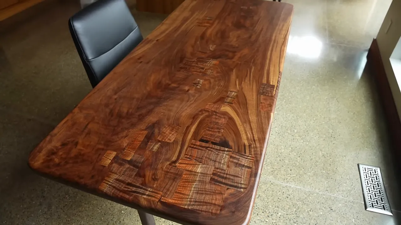 Completed walnut patchwork desk with rounded corners and a black chair beside it