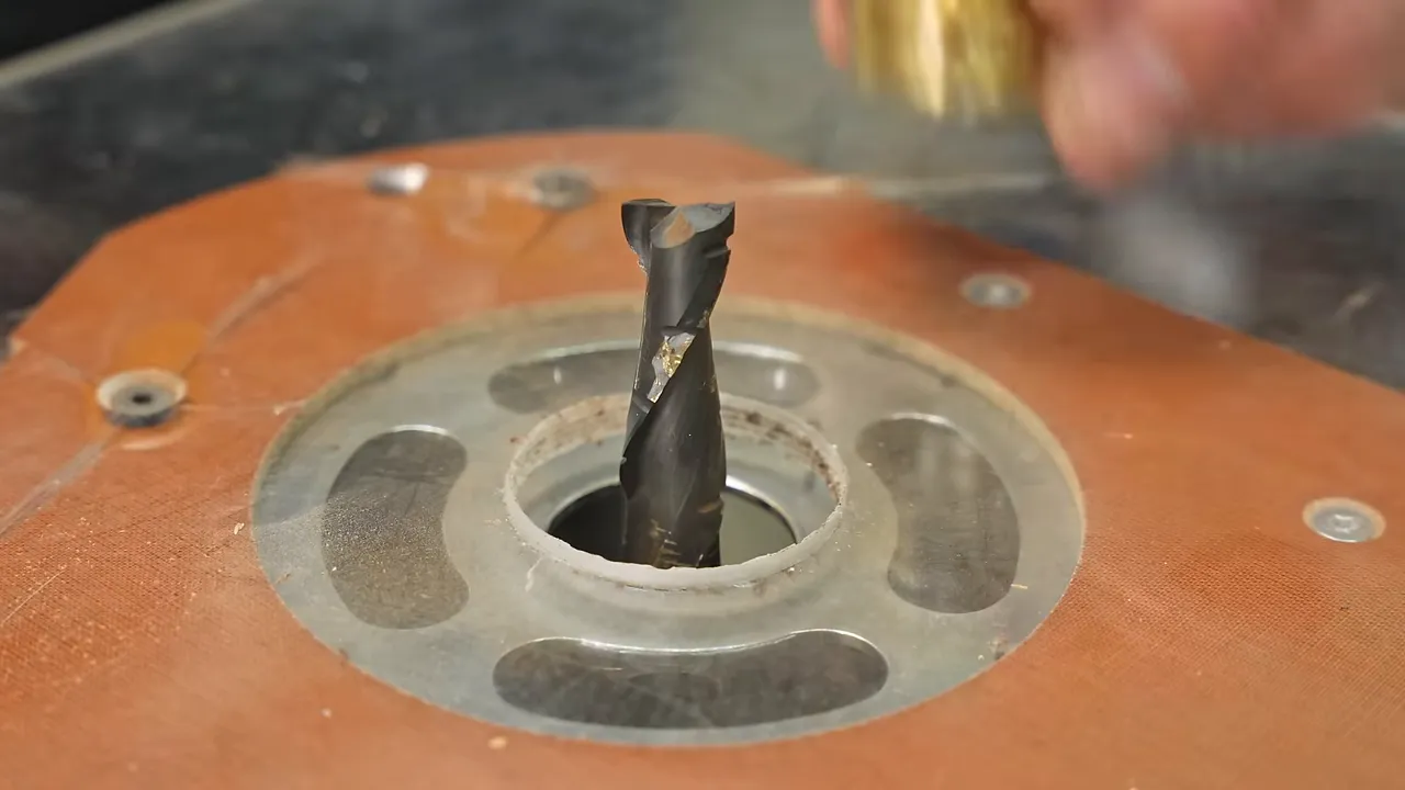 Damaged brass guide bushing held beside a spiral router bit and acrylic router base