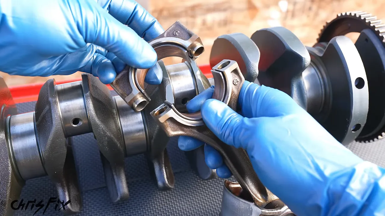Blue-gloved hands positioning a connecting rod and bearing cap around a crankshaft journal