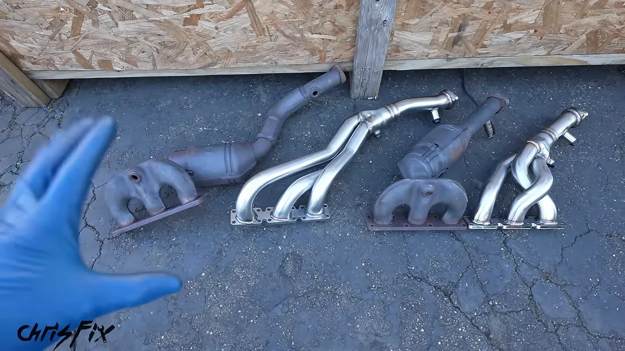 Two stock exhaust manifold assemblies laid beside two stainless steel tubular headers
