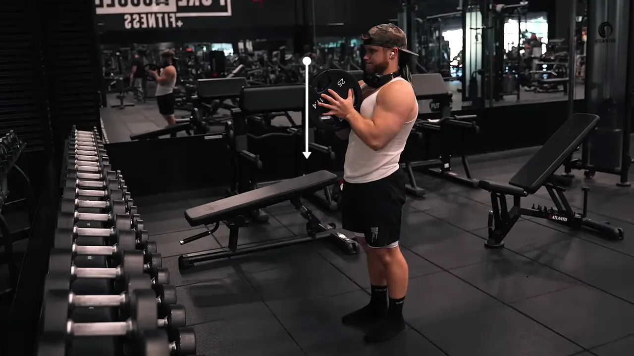 Lifter holding a weight plate in front of his chest with a white arrow pointing downward