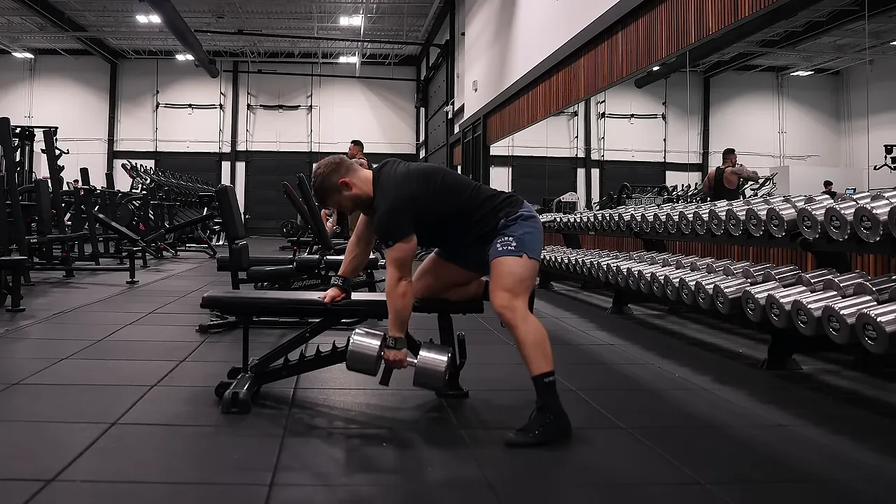 Lifter rowing a dumbbell with a wide stance and the opposite hand supported on a bench