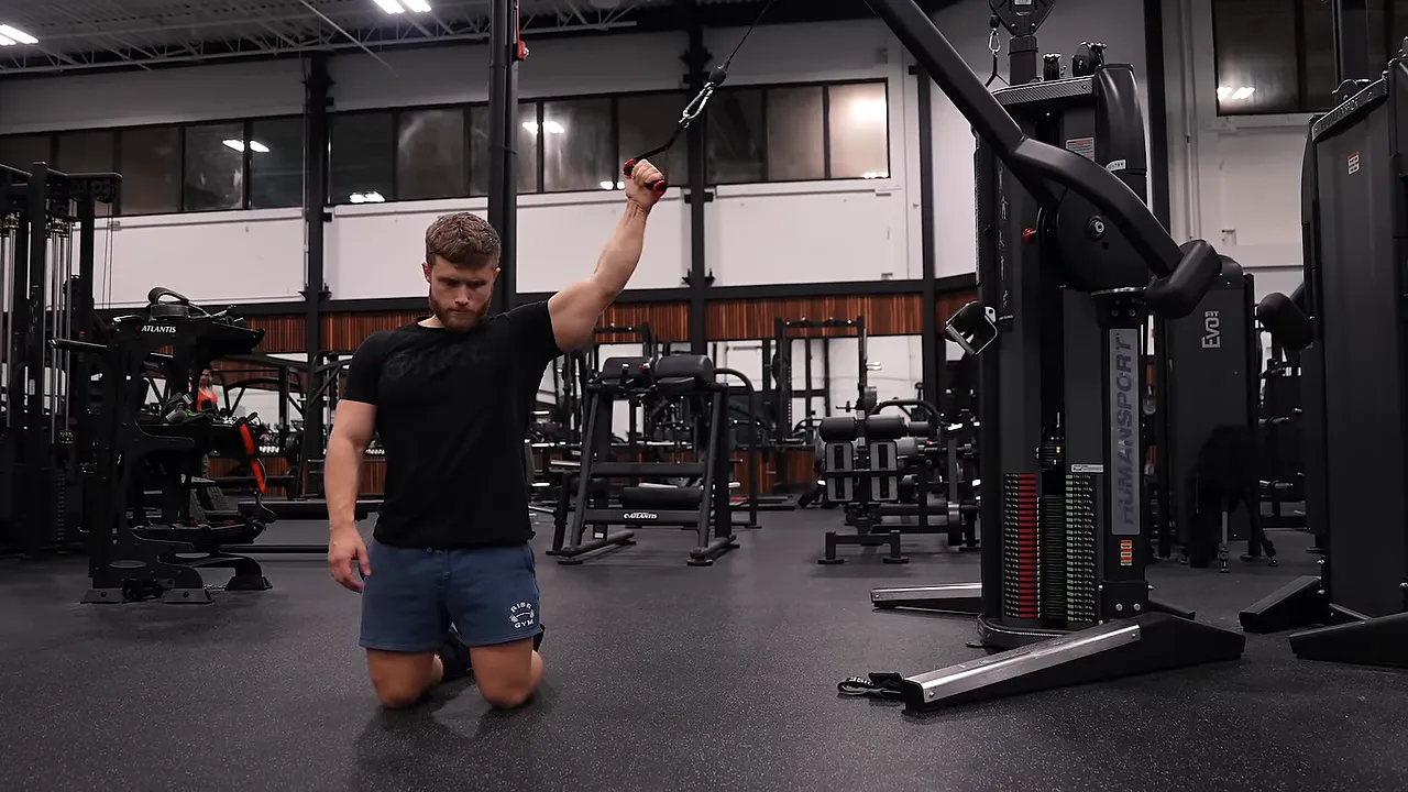 Kneeling lifter curling a cable handle toward his head with the working upper arm raised