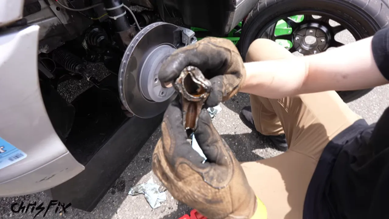 Gloved hands holding a broken connecting rod beside the BMW front brake rotor