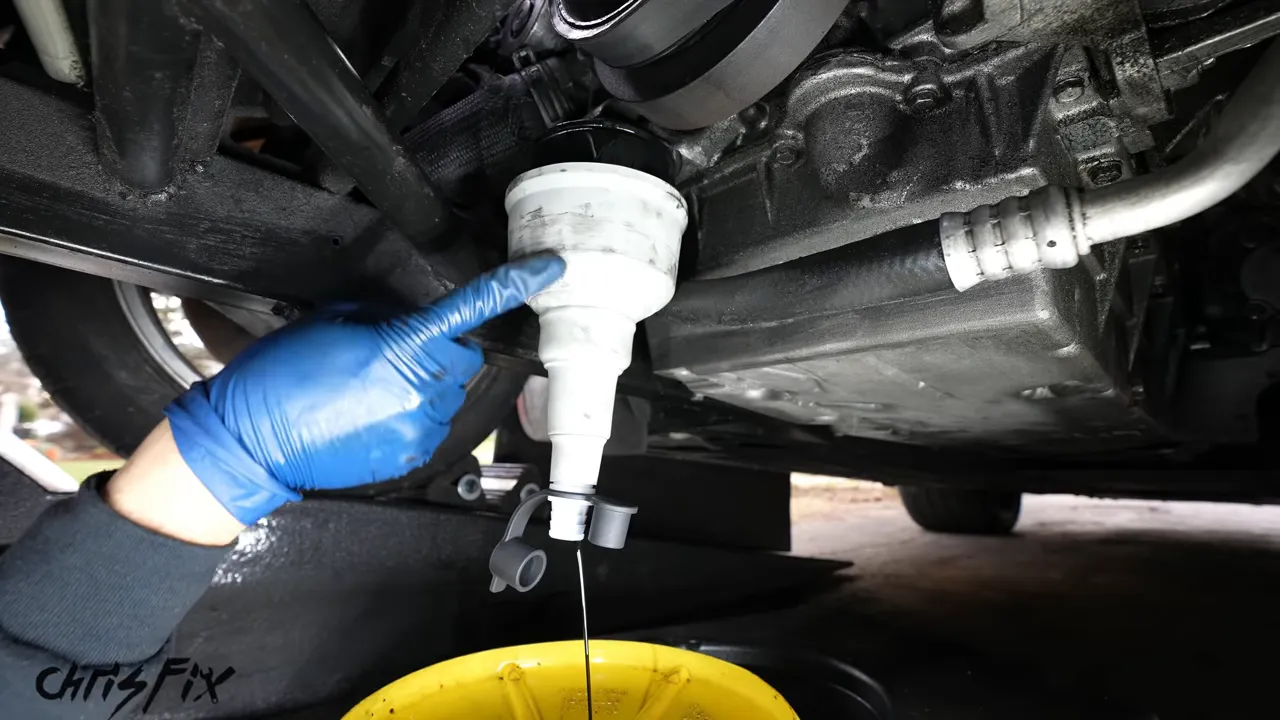 Oil Udder fitted over an oil filter with a hose leading toward a yellow drain container