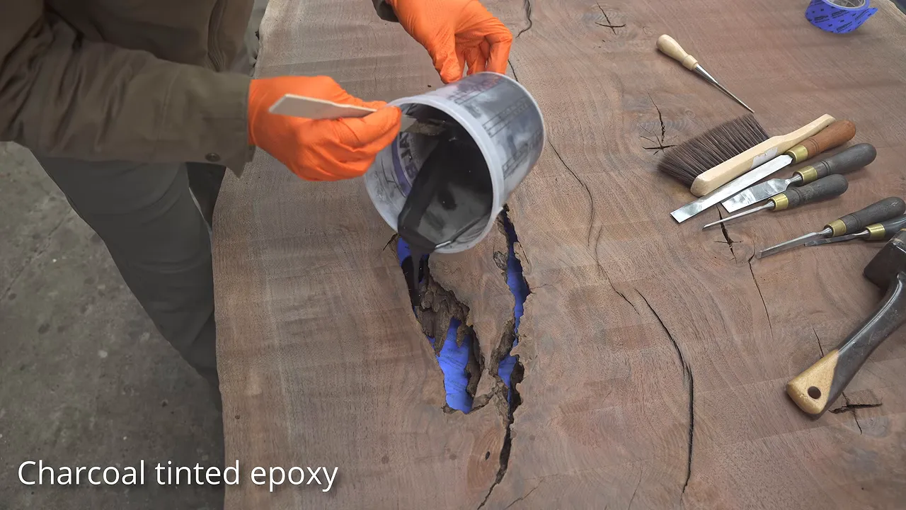 Charcoal-colored epoxy being poured into a crack backed with blue tape