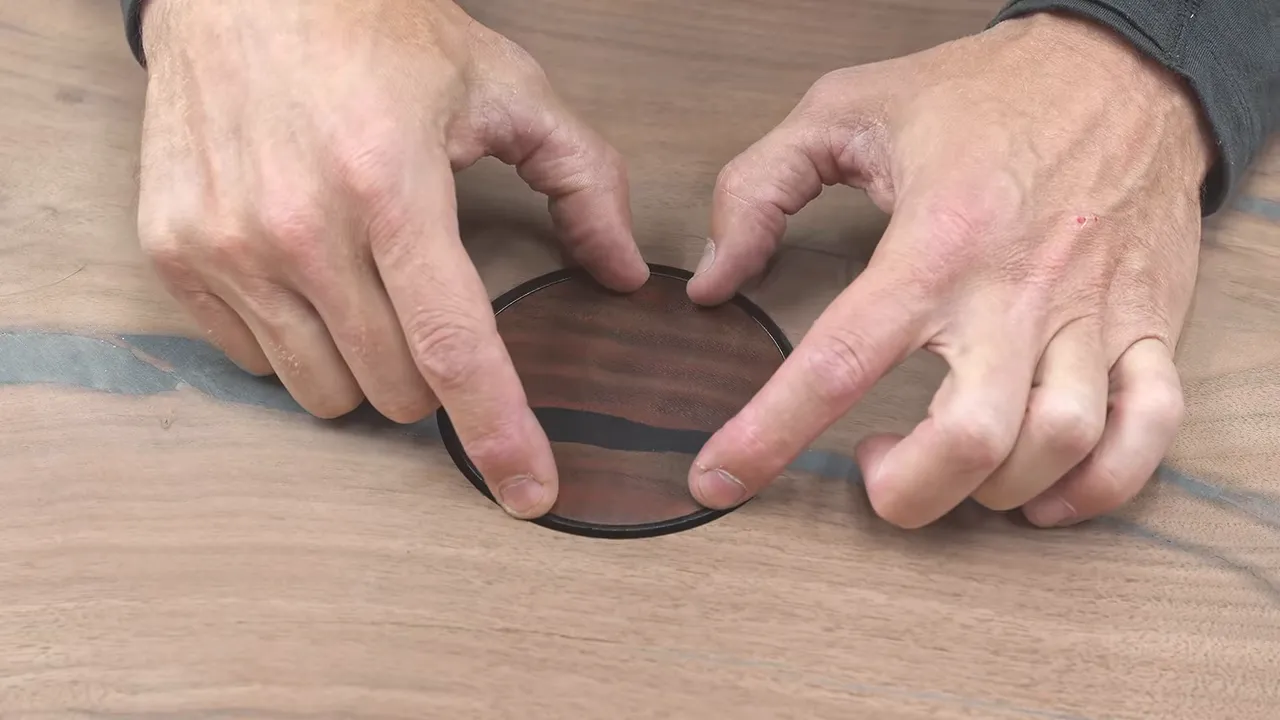 A round wooden outlet cover with a dark resin line aligned to the crack in the tabletop
