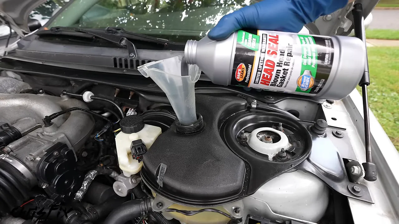 Head gasket sealer being poured through a funnel into the Jaguar’s coolant reservoir